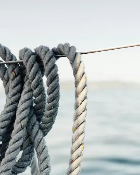 Des cordages lovés sur une filière, la mer grise derrière