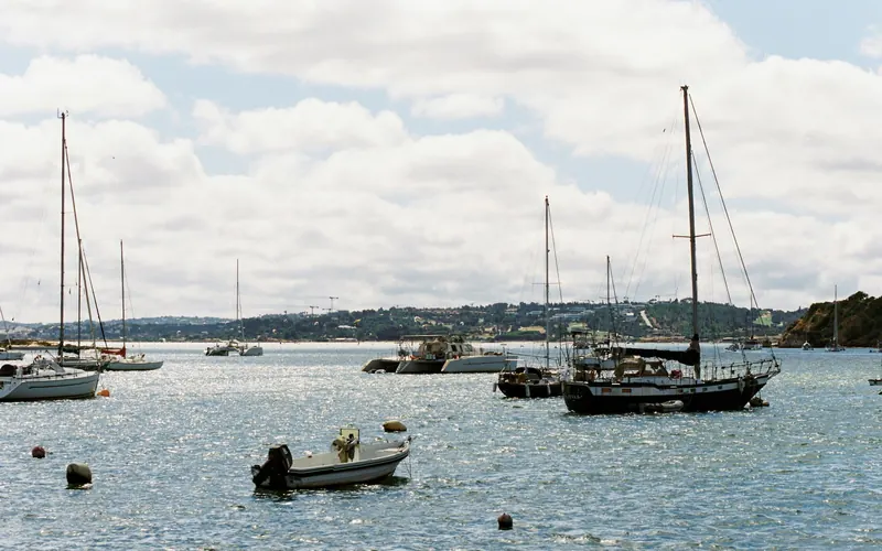 Des voiliers au mouillage dans l’estuaire, une petite vedette au premier plan, la rive boisée au fond